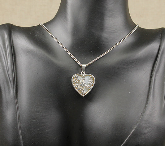 A silver heart-shaped pendant necklace with mother of pearl details, displayed on a mannequin.