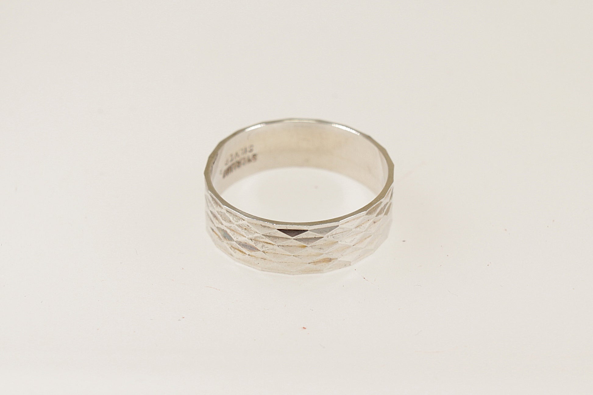 A silver band ring with an engine turned pattern, displayed against a white background.