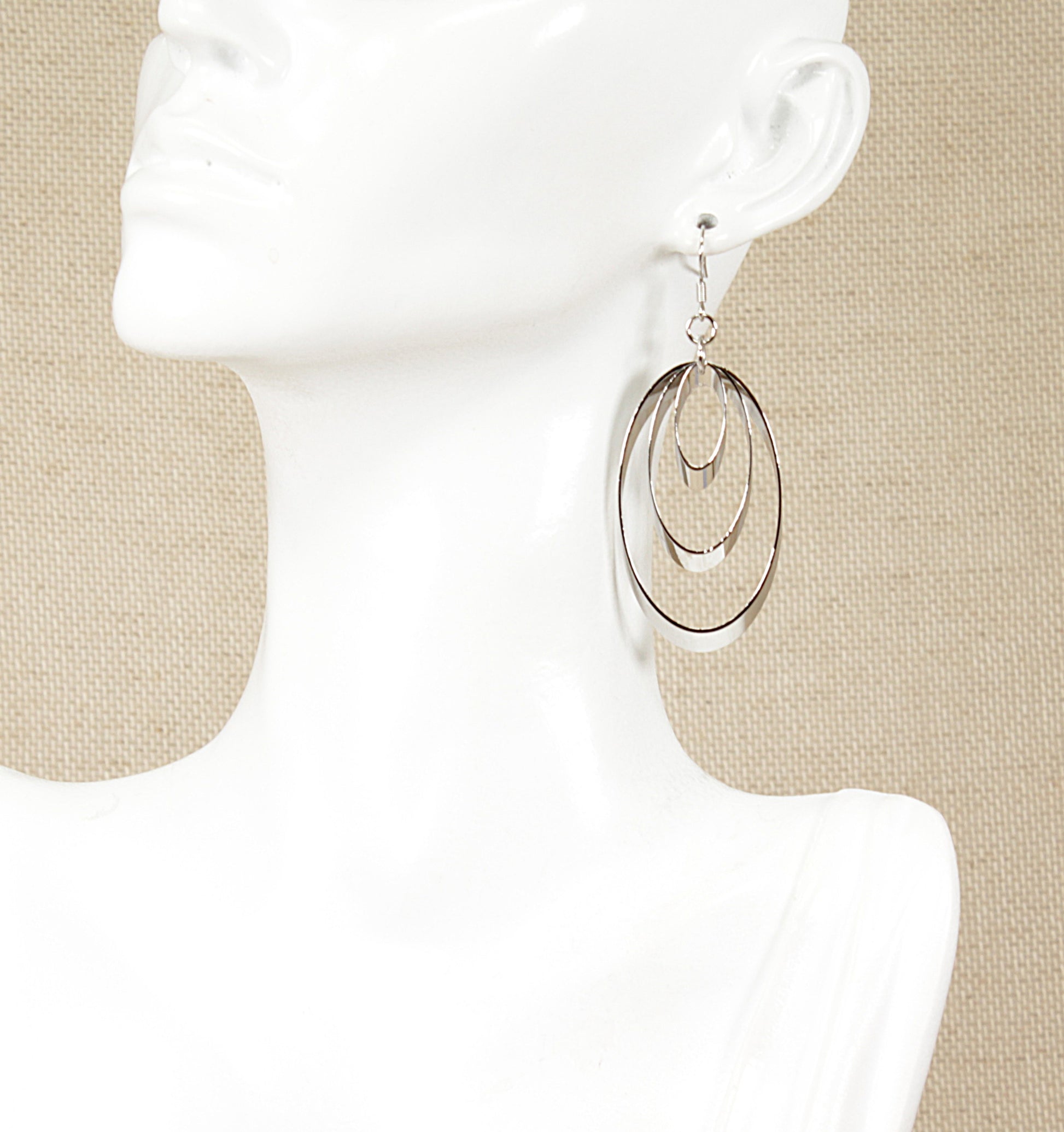 A pair of silver drop earrings with a trio of oblong rings on a mannequin head.