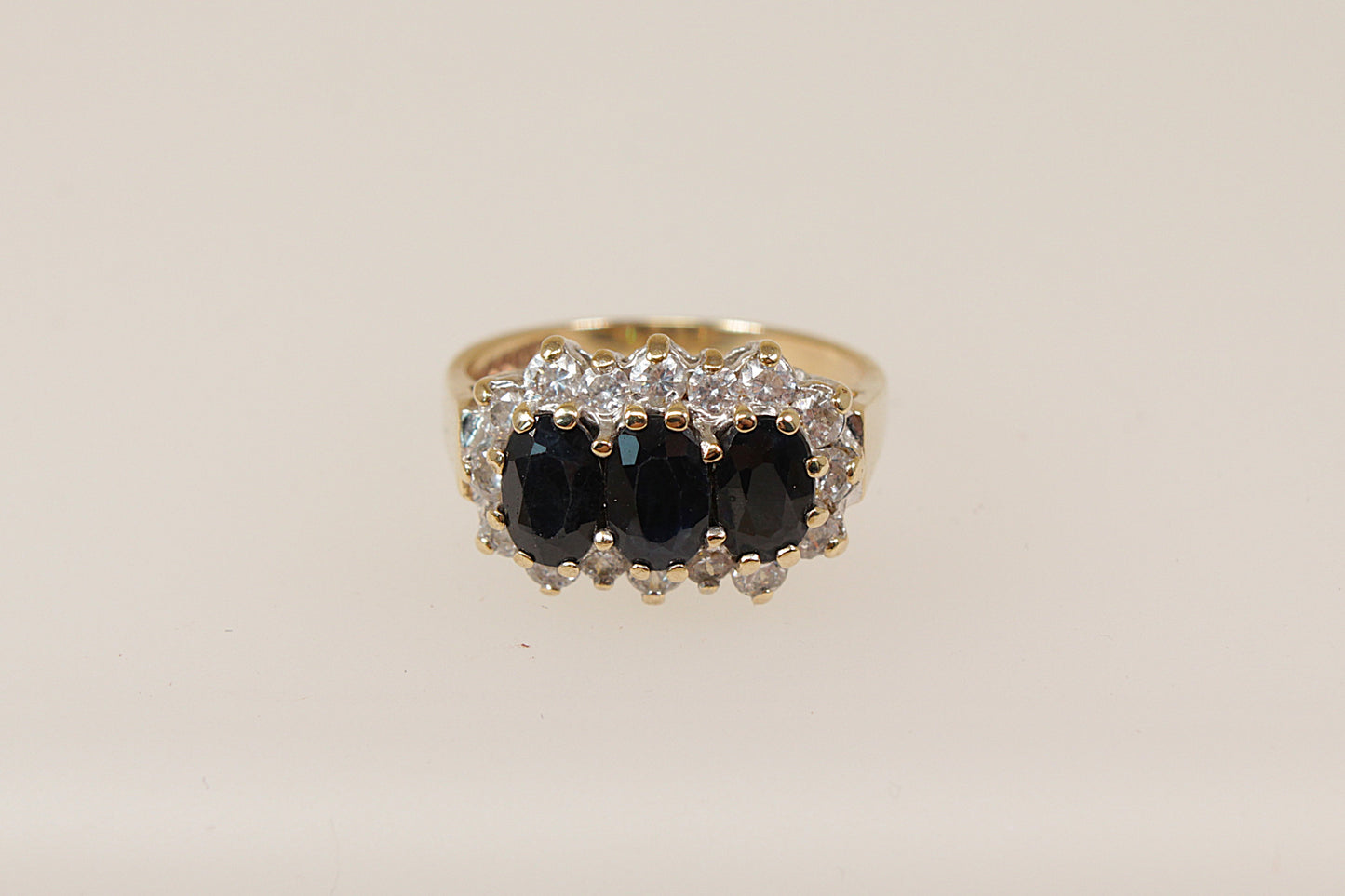 A vintage 9ct gold sapphire trilogy ring with claw set oval blue sapphires and cubic zirconia gemstones around the mount, on a white background.