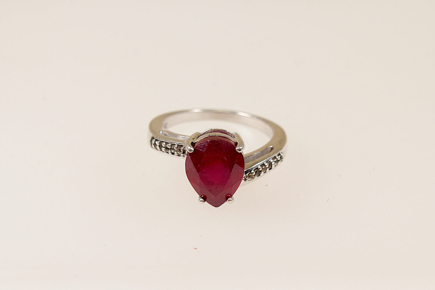 A sterling silver pear shaped ruby solitaire with white topaz accents on each shoulder, Stamped 925 for sterling silver and the makers mark ‘TGGC’ for The Genuine Gemstone Company, UK finger size J.