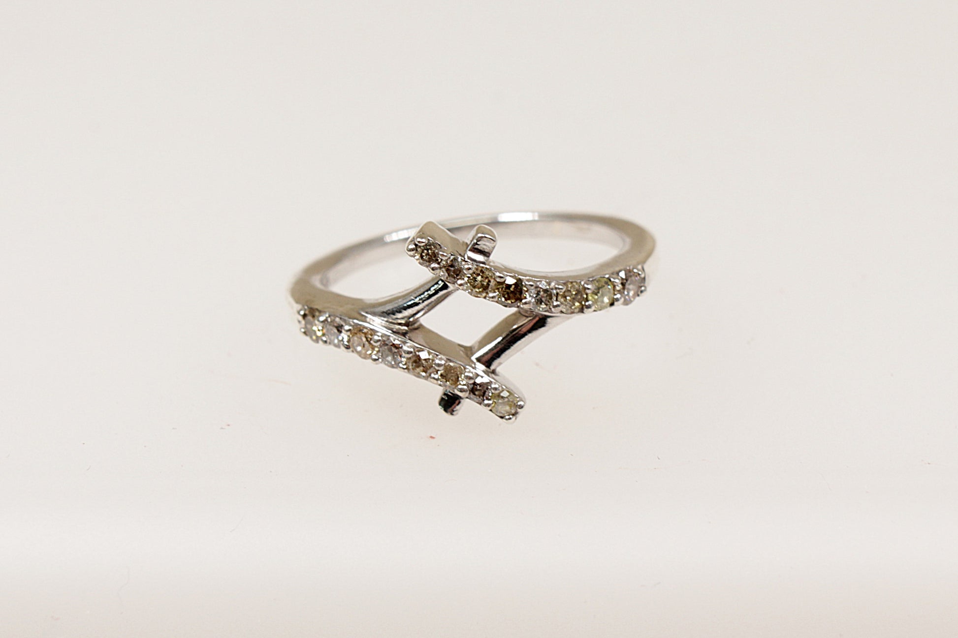 A silver diamond ring with two crossover bands, featuring claw set diamond gemstones on a white background.