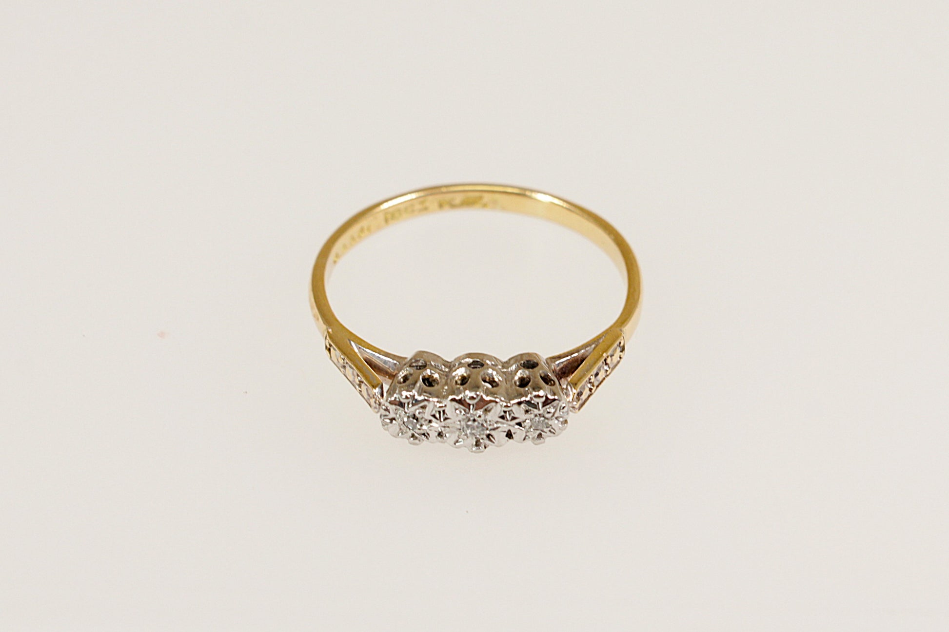 An 18ct Gold and Platinum Diamond Trilogy Ring with a central larger diamond flanked by two smaller diamonds on each side, set against a white background.