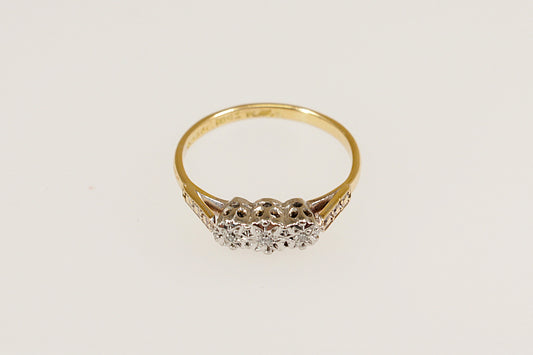 An 18ct Gold and Platinum Diamond Trilogy Ring with a central larger diamond flanked by two smaller diamonds on each side, set against a white background.