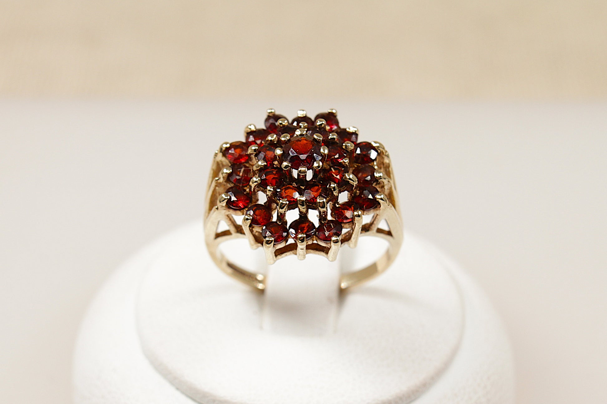 A 9ct gold garnet cluster ring with multiple garnet stones arranged in a circular pattern in the center, displayed on a white mount.