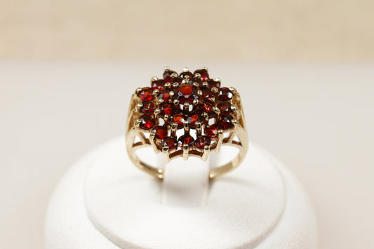 A 9ct gold garnet cluster ring with multiple garnet stones arranged in a circular pattern in the center, displayed on a white mount.