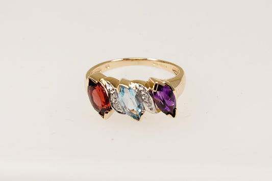 This pretty and unique piece of jewellery is handcrafted in 9ct Gold and features 3 Marquis cut gems that are interspaced with Diamond accents. The gemstones are Garnet, Blue Topaz and Amethyst, these are arranged on a slant, creating a dynamic, stylish appearance. There are 4 diamond accents enhancing the rings sparkle and sophistication. UK finger size O.