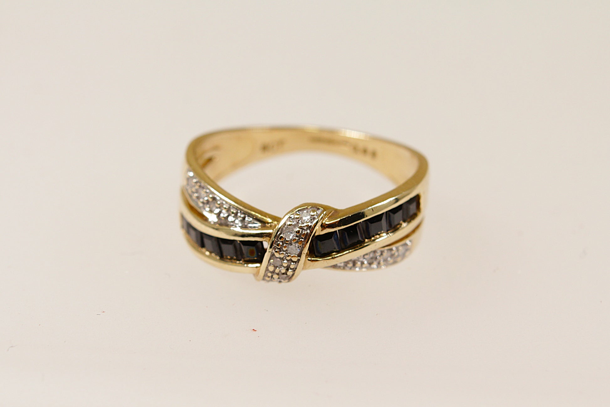 A 9ct gold ring with a bow design, featuring channel set blue sapphires along the loops and claw set round diamonds along the ribbon, displayed against a white background.