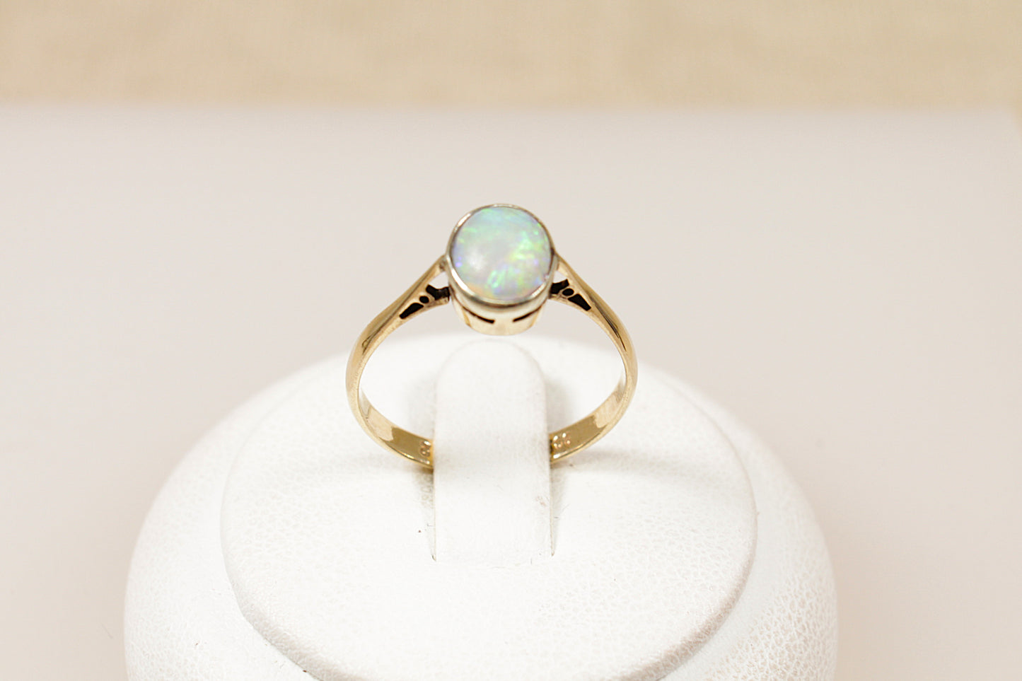 A vintage 9ct gold solitaire ring with an oval-shaped opal centerpiece displayed on a white stand.