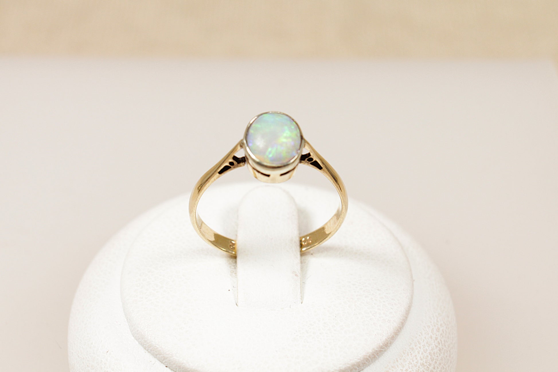 A vintage 9ct gold solitaire ring with an oval-shaped opal centerpiece displayed on a white stand.