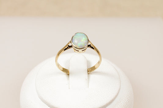 A vintage 9ct gold solitaire ring with an oval-shaped opal centerpiece displayed on a white stand.