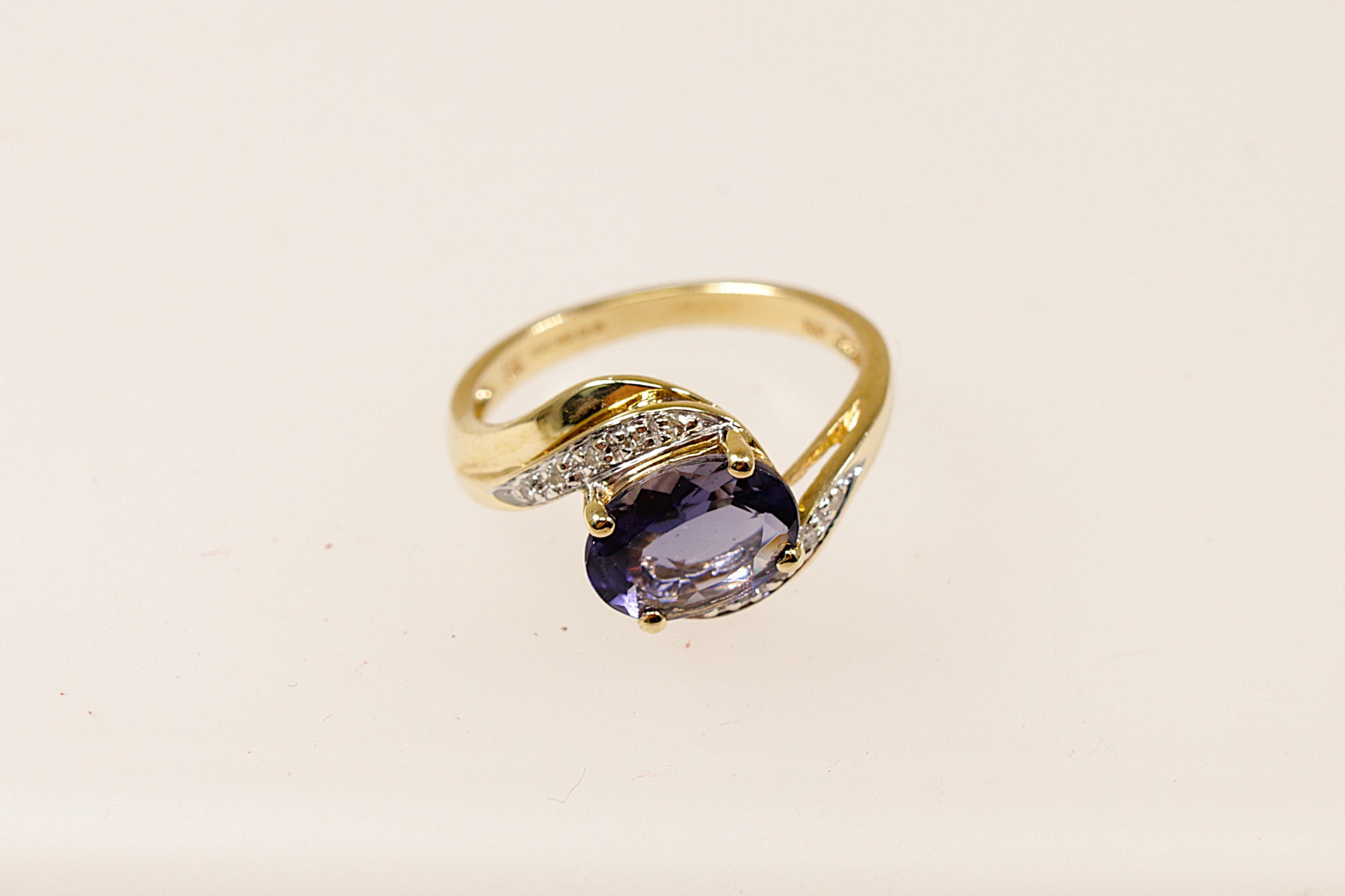 This 9ct Gold ring is a perfect blend of classic and contemporary design. The combination of the rich Iolite, shimmering Diamond accents, and the fluid twist design creates a piece that feels both timeless and distinctive. The centrepiece is the oval Blue Iolite that is claw set across the setting that gives a modern touch to the classic twist design. The Diamond accents are set along the twist. UK finger size M.