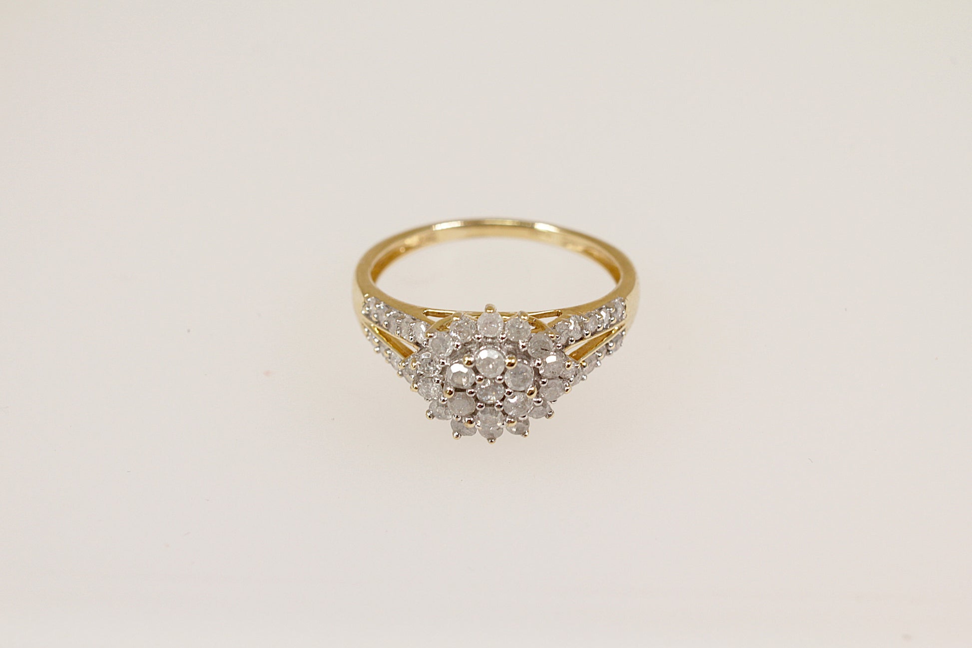 A 9ct gold diamond cluster ring with a two-tiered floral design, featuring a central flower-shaped cluster with sparkling diamonds and diamond accents on the shoulders.
