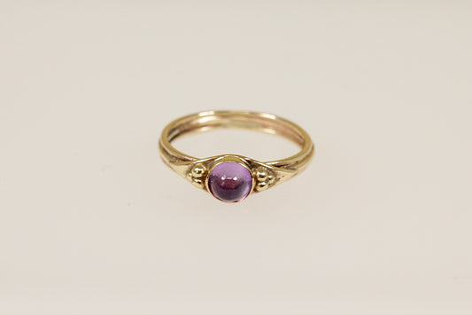 A vintage gold ring with a round amethyst cabochon gemstone set in a 9ct gold band with hallmarks interior.