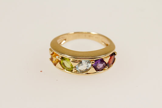 A 9ct gold ring with multiple oval gemstones set in a line on the top, including citrine, peridot, white topaz, garnet, and amethyst. UK finger size M.