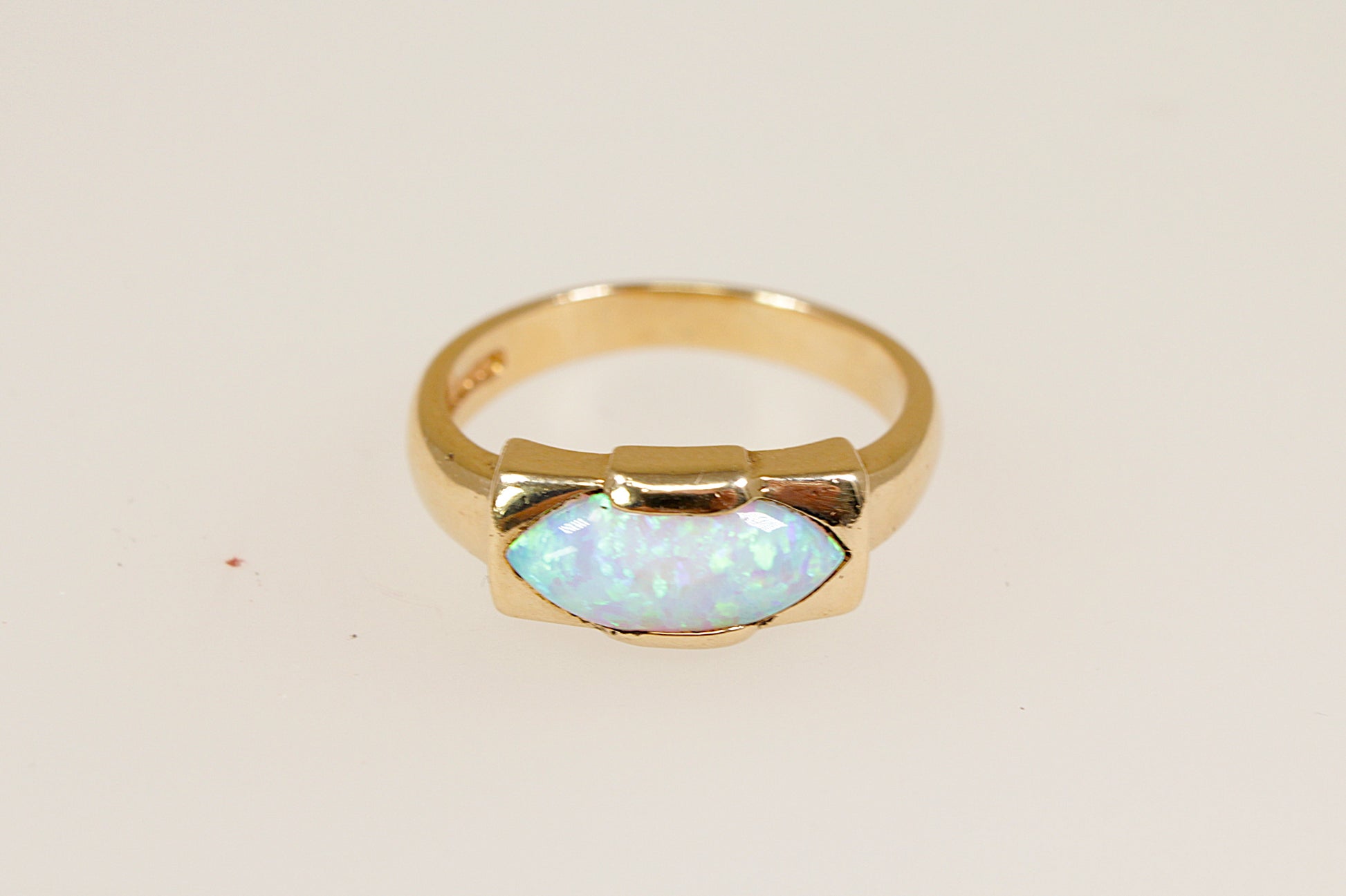 A 9ct gold ring with an opal centerpiece set in a rectangular bezel, displaying vibrant orange, red, and yellow hues against a white background. UK finger size O.