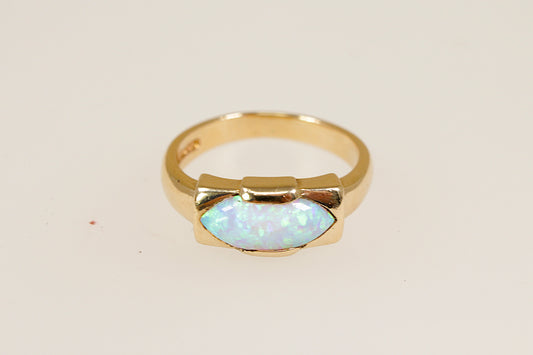 A 9ct gold ring with an opal centerpiece set in a rectangular bezel, displaying vibrant orange, red, and yellow hues against a white background. UK finger size O.