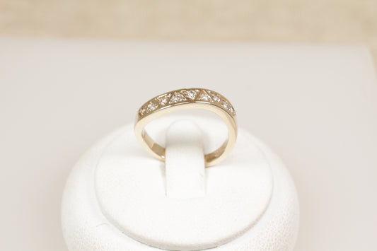A 9ct gold diamond eternity ring displayed on a white mount, featuring triangular diamond formations and a wave effect band.