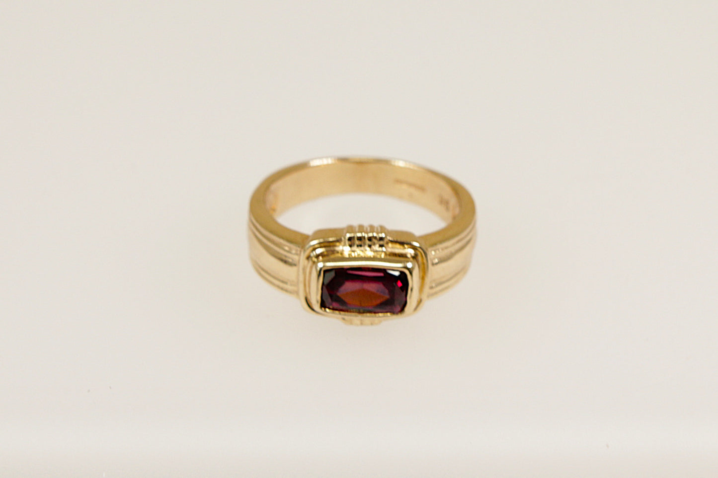 A 9ct gold ring with a rectangular Rhodolite Garnet set horizontally across a raised head, bezel set for a sleek and secure look, with Art Deco inspired goldwork elements. UK finger size N.