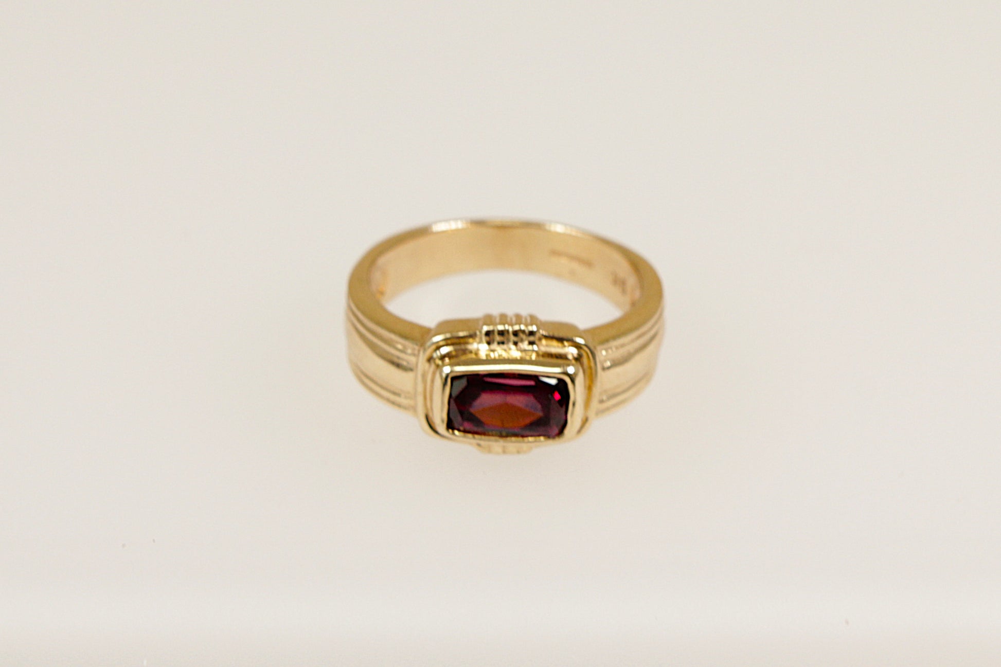 A 9ct gold ring with a rectangular Rhodolite Garnet set horizontally across a raised head, bezel set for a sleek and secure look, with Art Deco inspired goldwork elements. UK finger size N.