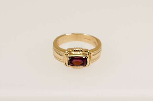 A 9ct gold ring with a rectangular Rhodolite Garnet set horizontally across a raised head, bezel set for a sleek and secure look, with Art Deco inspired goldwork elements. UK finger size N.