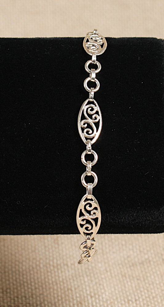 A silver filigree bracelet with oval, filigree designed links, displayed against a black background.