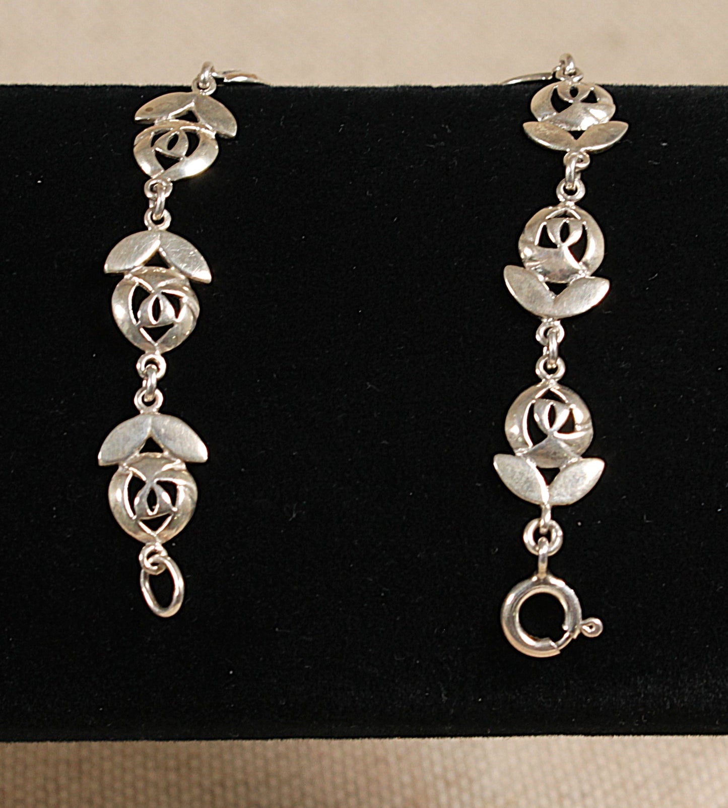 A silver bracelet with floral inspired design, featuring links shaped like flowers with two petals and a flower head, displayed against a black background.