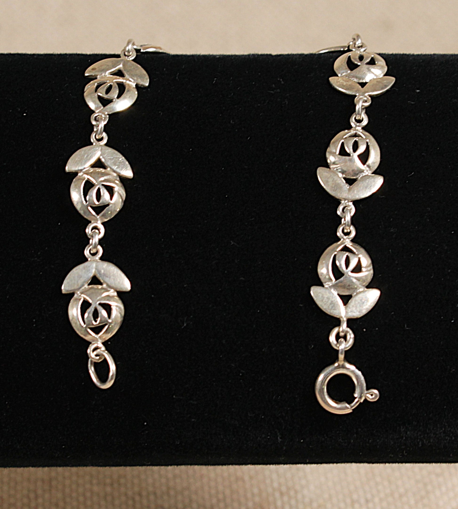 A silver bracelet with floral inspired design, featuring links shaped like flowers with two petals and a flower head, displayed against a black background.