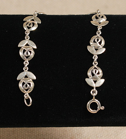 A silver bracelet with floral inspired design, featuring links shaped like flowers with two petals and a flower head, displayed against a black background.