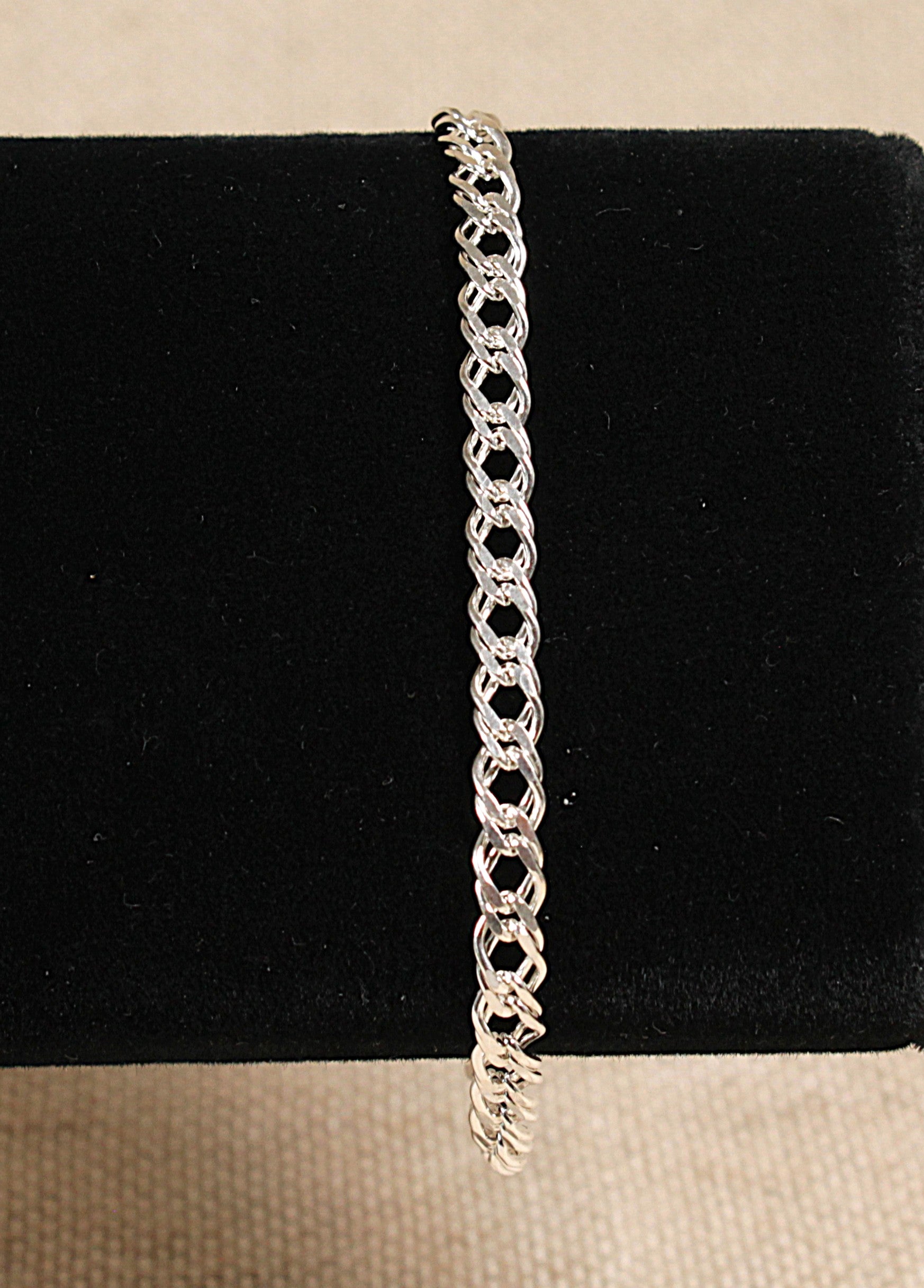 A silver chain link bracelet with a double link design and a lobster clasp fastening, displayed on a black stand.