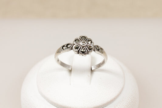 A vintage silver ring with a daisy design, featuring marcasite stones on the flower head and shoulders, displayed on a white mount.