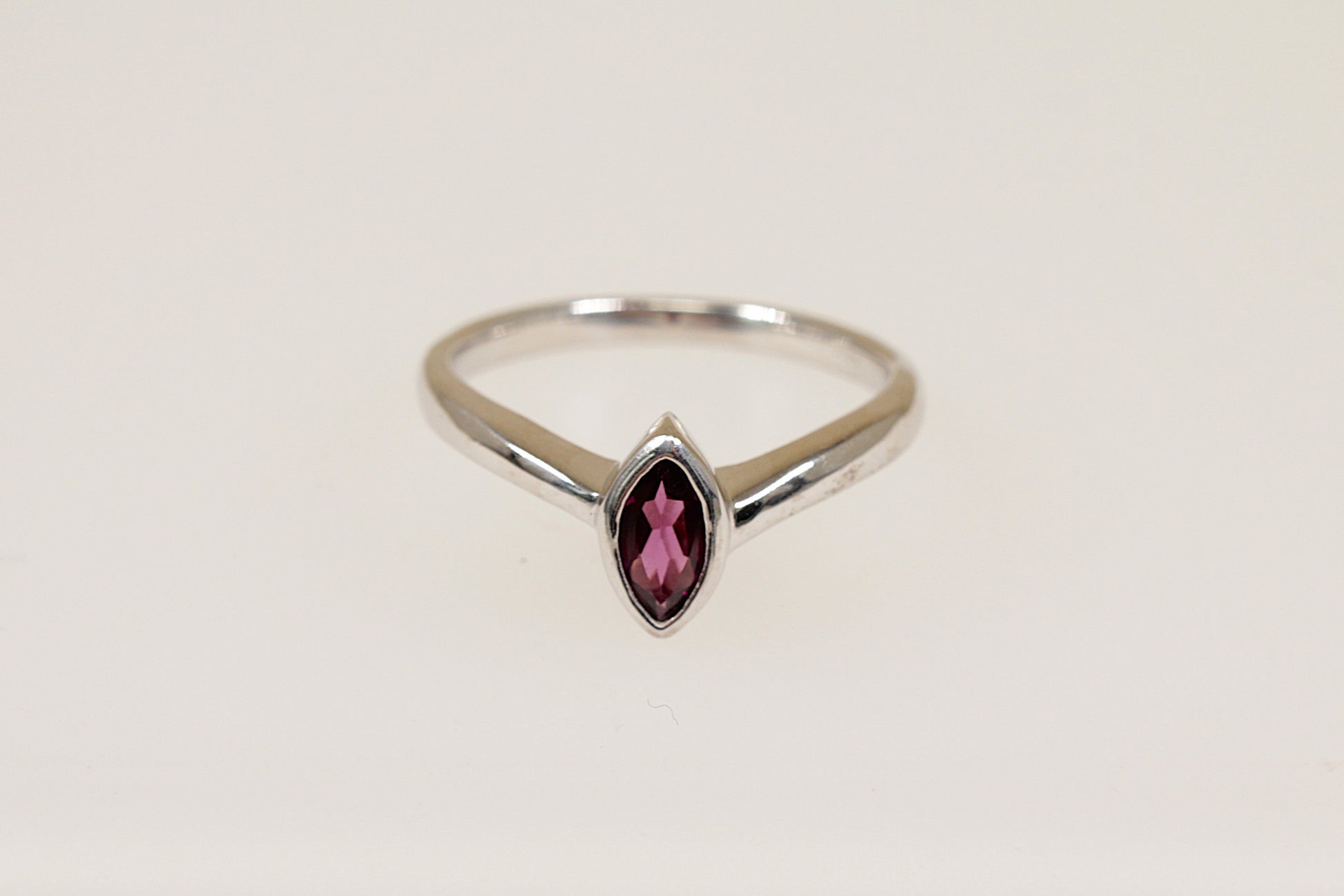 A marquise cut garnet ring with a bezel setting, in silver color, with a white background.