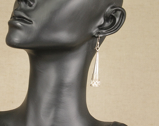 A pair of silver drop earrings with ornate detailing, displayed on a mannequin head.