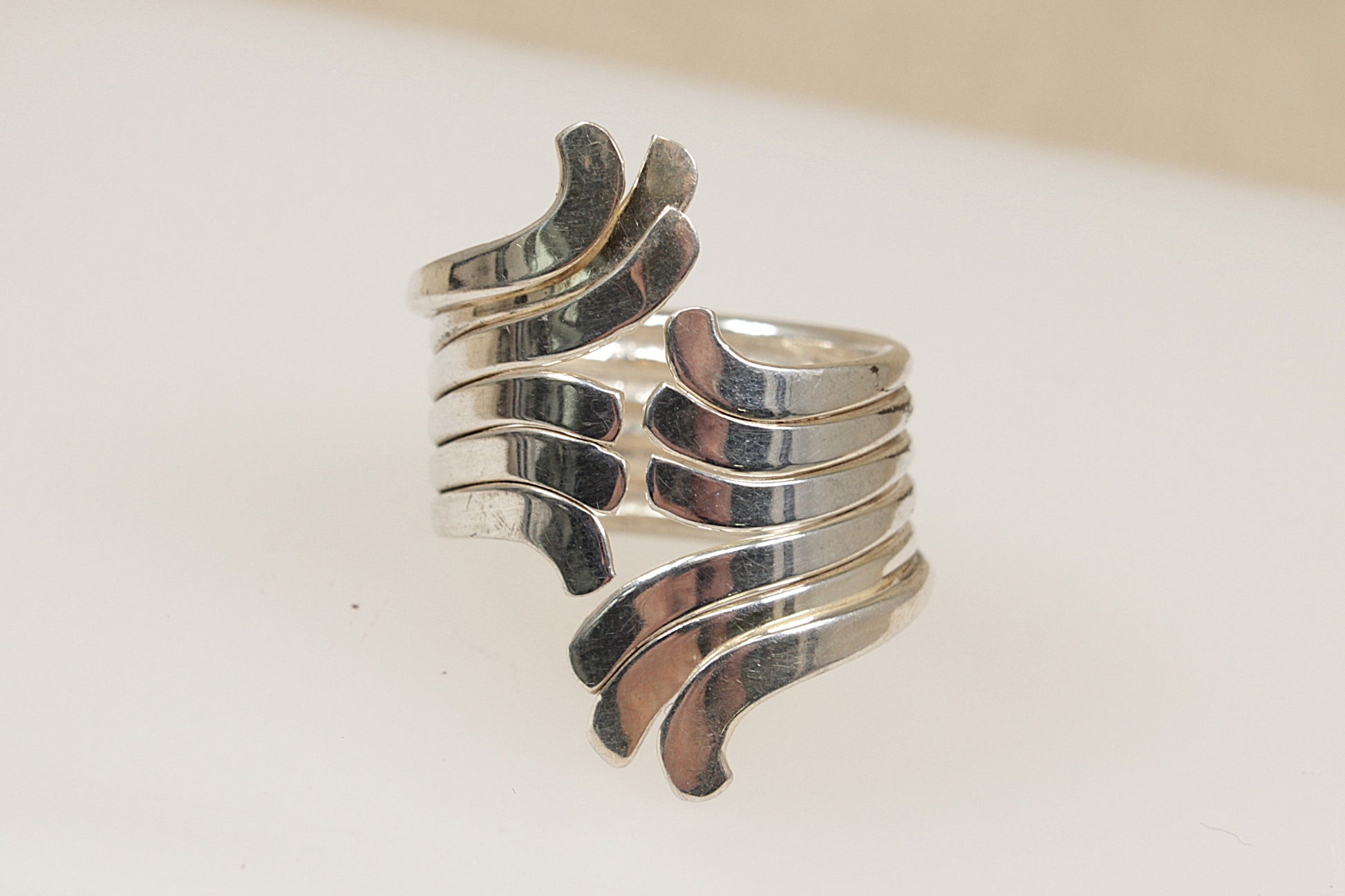 A silver statement ring with multiple bands forming a sculptural effect on a white background.