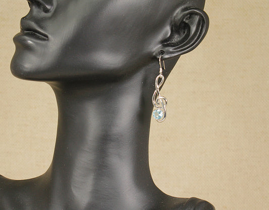 A pair of silver drop earrings with blue topaz stones displayed on a mannequin head.