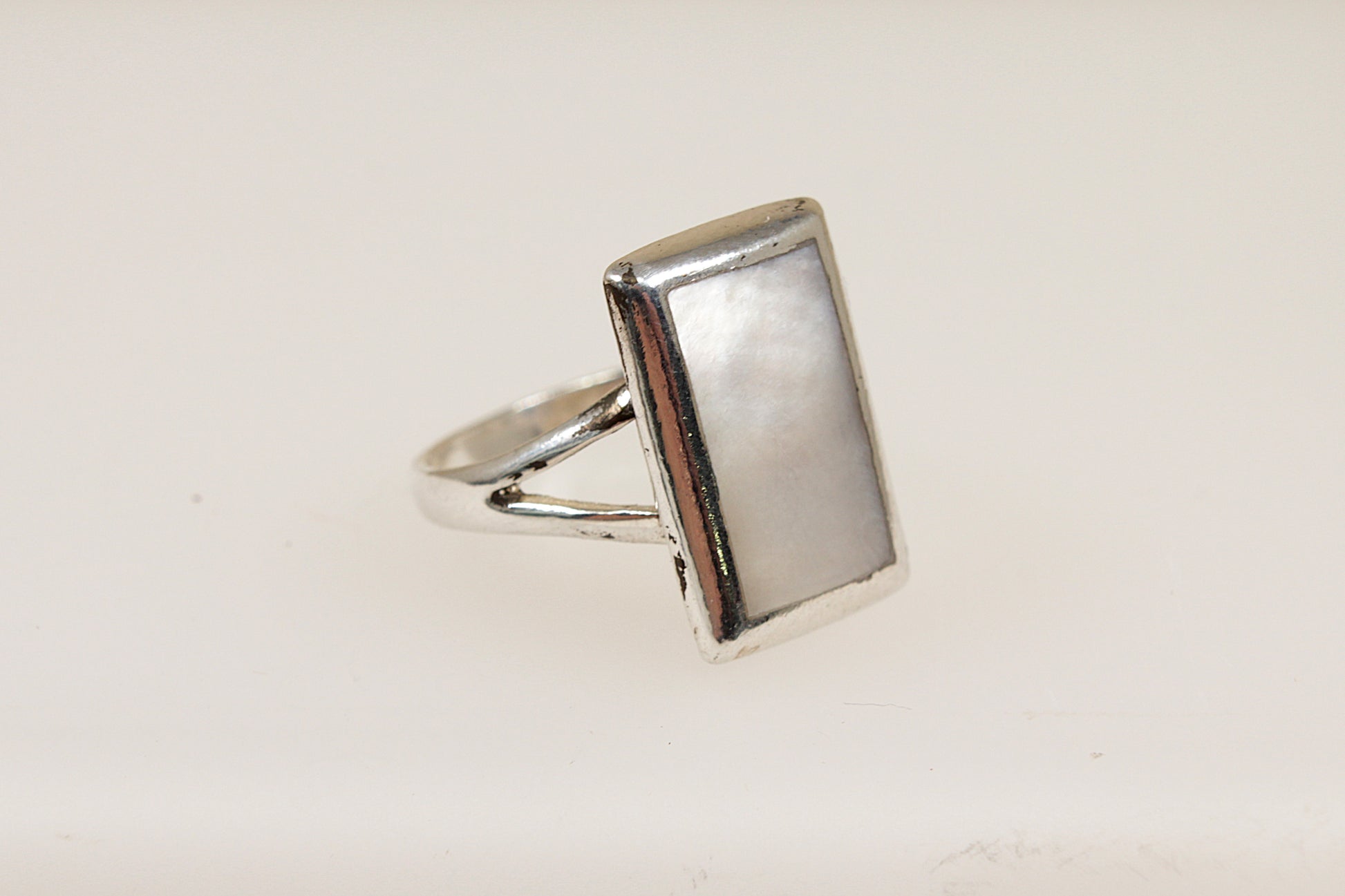 A silver ring with a rectangular mother of pearl inlay against a white background.