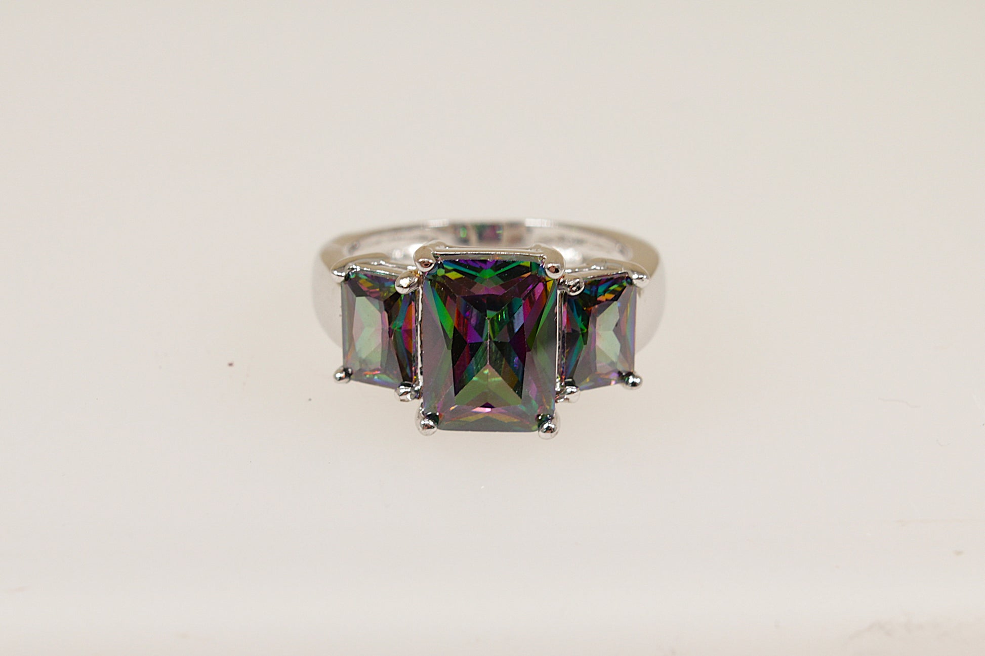 An elegant sterling silver ring with a central emerald cut mystic crystal gemstone, flanked by two smaller side stones, set in a crown setting.