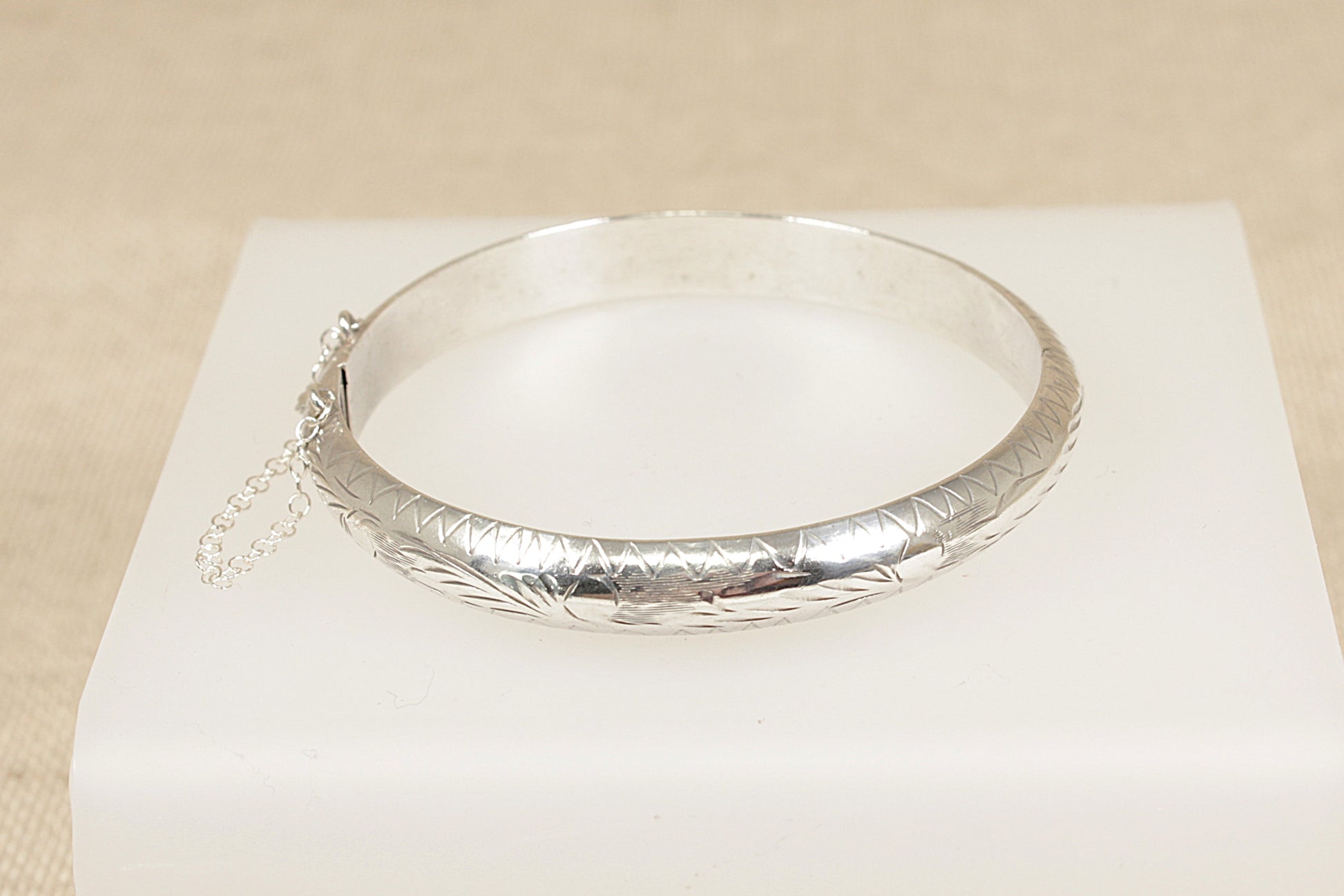 Silver bracelet hinged bangle on a white box with a beige background 