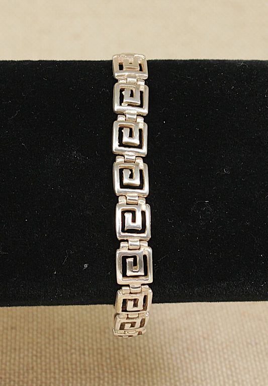 A silver bracelet with a Greek Key design, featuring square articulated links, displayed on a black background.
