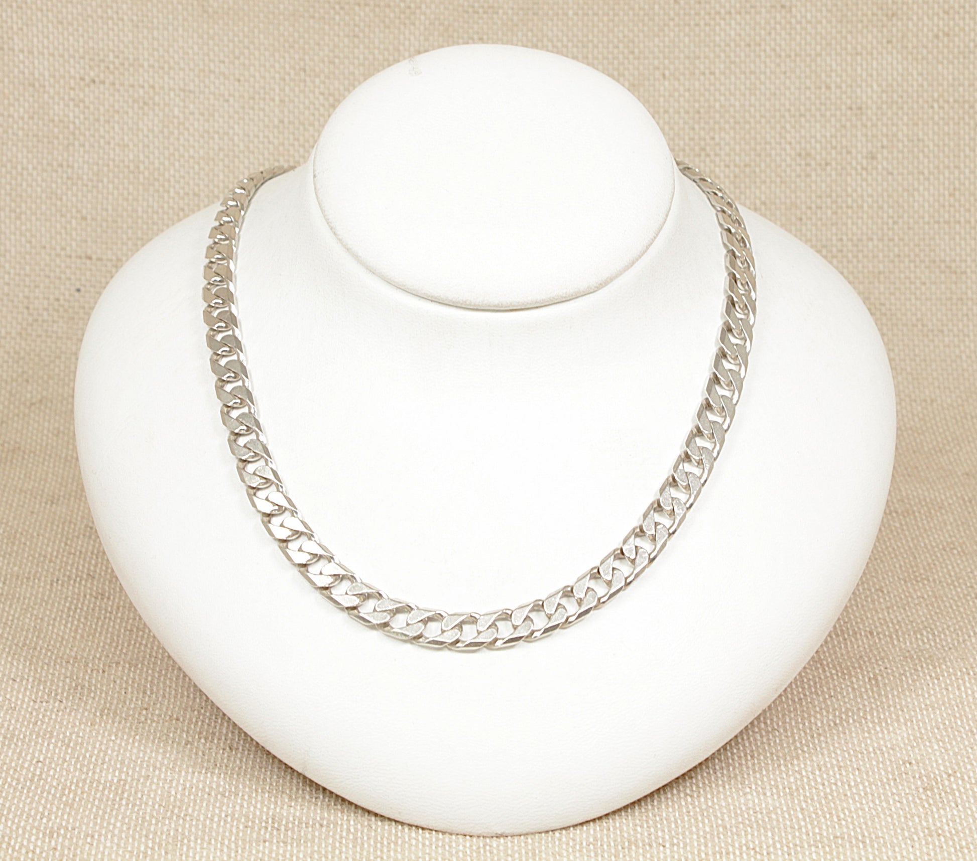 A silver curb link necklace displayed on a white mannequin bust against a beige background.