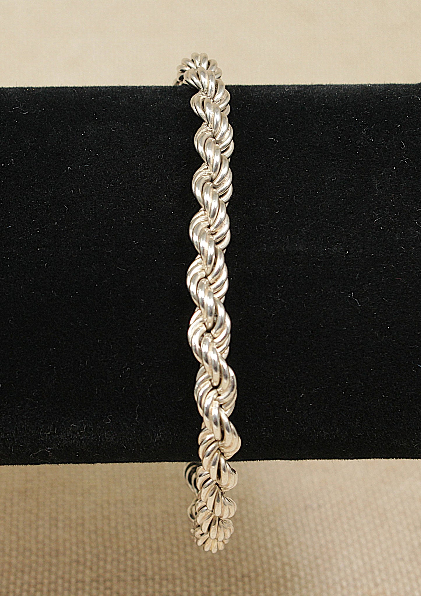 A silver rope link bracelet with a round bolt clasp, displayed on a black background.
