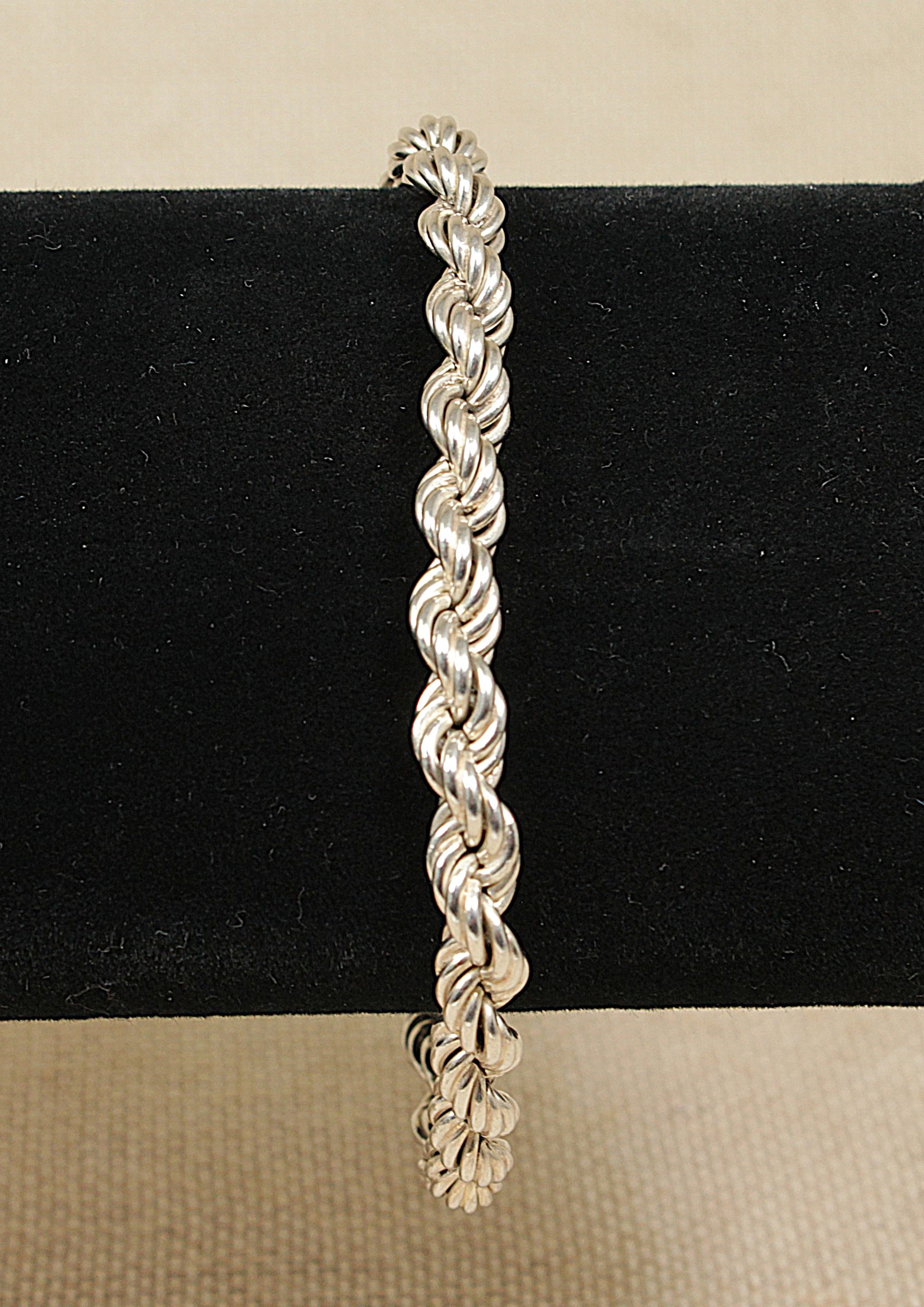 A silver rope link bracelet with a round bolt clasp, displayed on a black background.