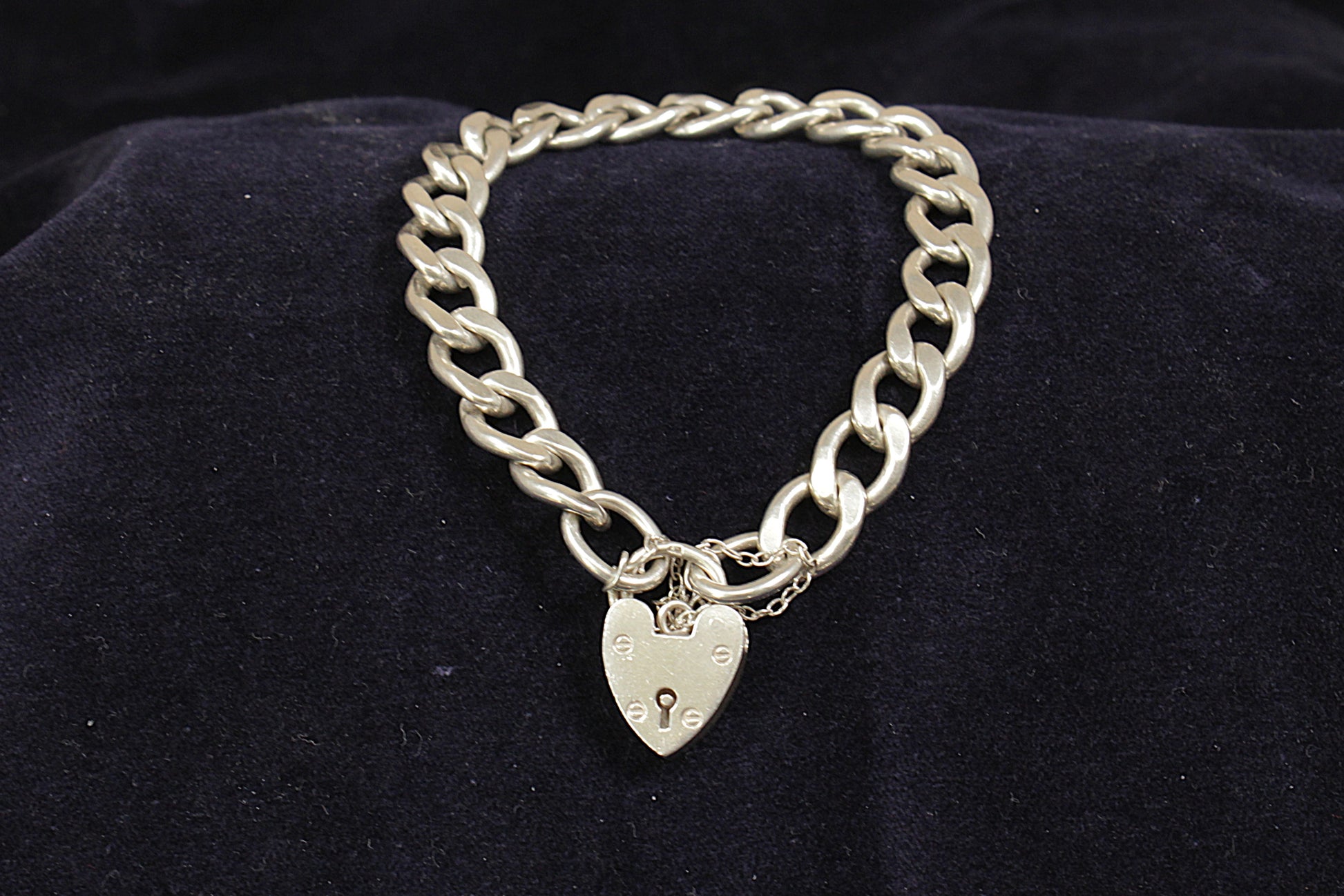 A vintage silver curb link bracelet with a padlock fastening and a safety chain, displayed on a black background.