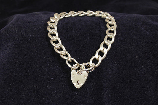 A vintage silver curb link bracelet with a padlock fastening and a safety chain, displayed on a black background.