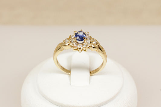 A timeless and elegant 9ct gold ring, inspired by the iconic Diana style. At its centre sits a rich oval sapphire, surrounded by a halo of 10 sparkling diamonds, creating a classic and regal look in a more delicate, wearable size, UK finger size P.