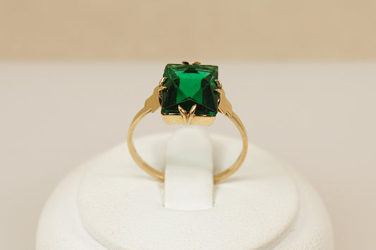Art Deco Vintage Gold ring with a green gemstone on a white stand against a beige background
