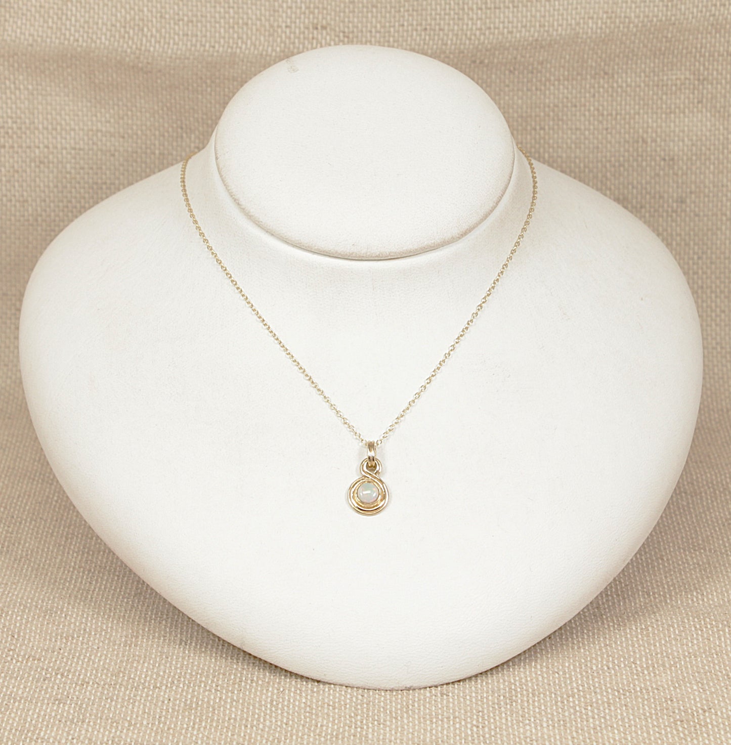 Gold necklace with a pendant on a white mannequin bust against a beige background