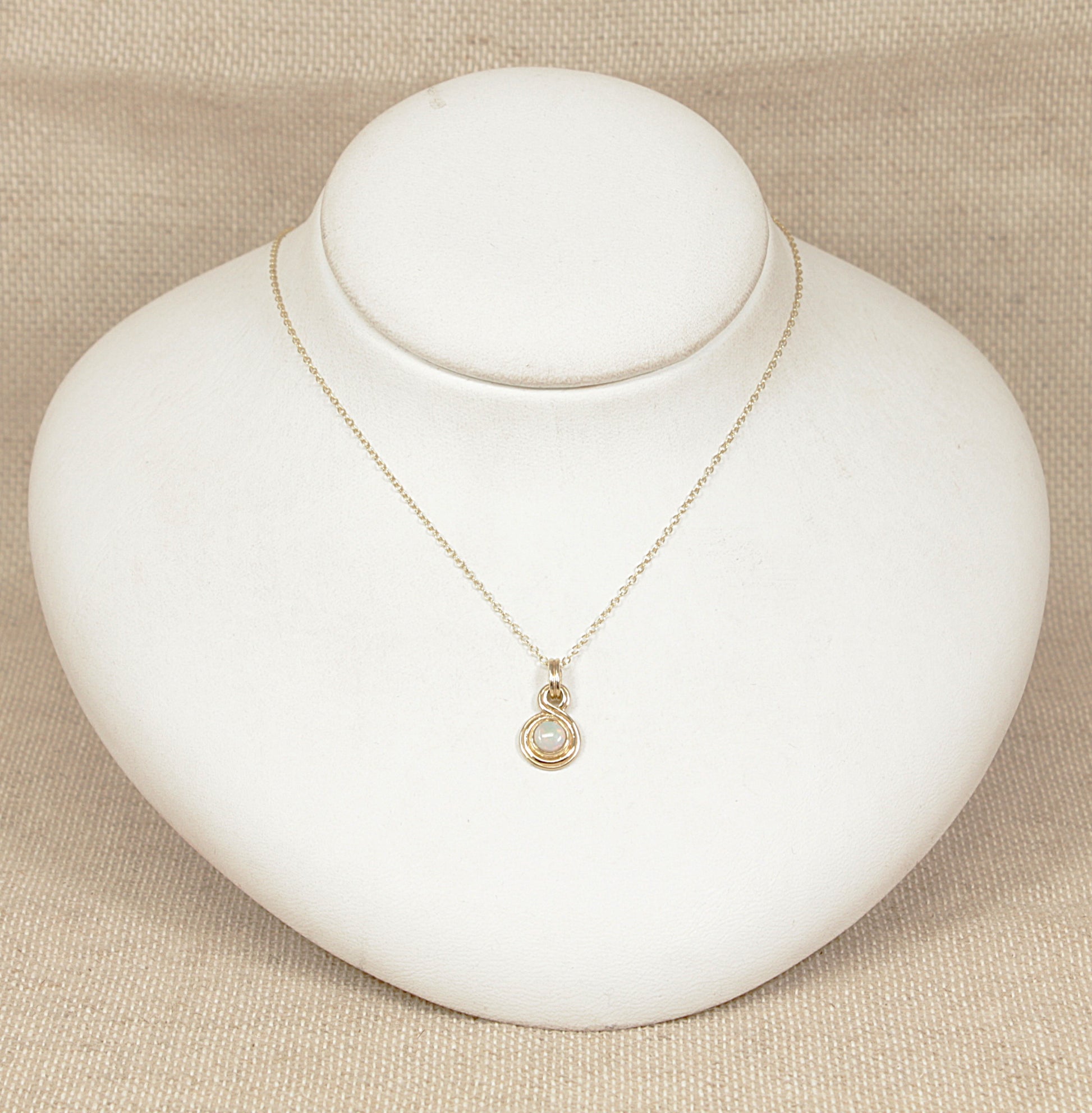 Gold necklace with a pendant on a white mannequin bust against a beige background