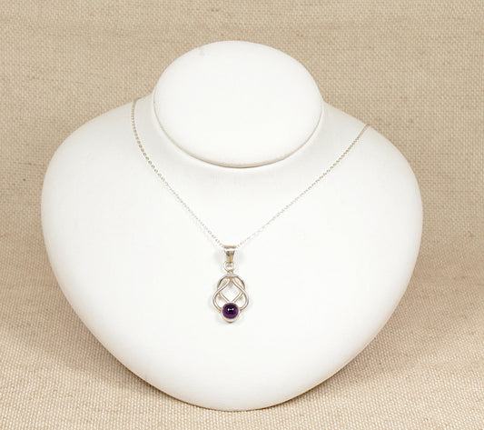 This beautiful and elegant Silver pendant has a timeless and meaningful knot design that suggests unity.
The round cabochon Amethyst at the bottom adds a lovely pop of colour, the bezel set amethyst allows its natural beauty to stand out whilst the bezel setting ensures that the gemstone is secure.
It sits on an 18 inch silver belcher design chain, both are stamped 925 for sterling silver.