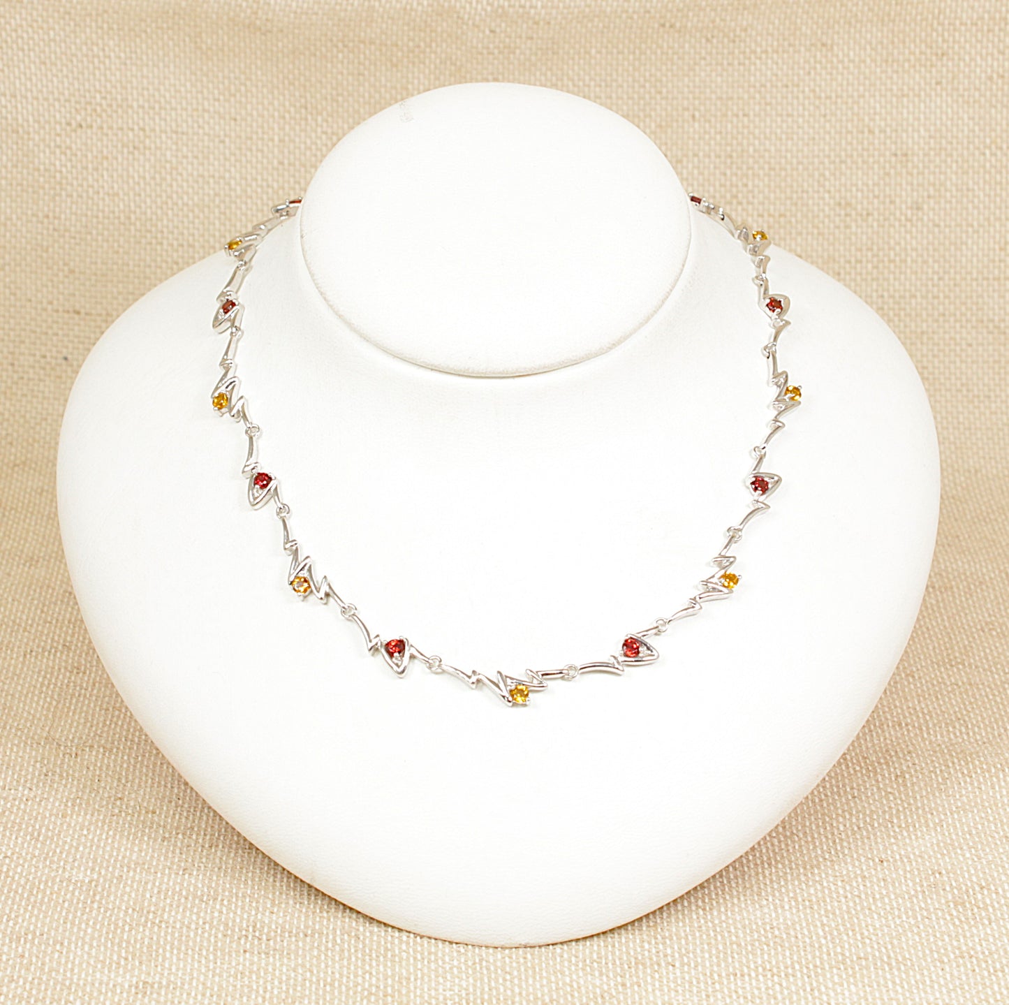 A sterling silver necklace with links set with alternating garnet and citrine gemstones on a white mannequin.